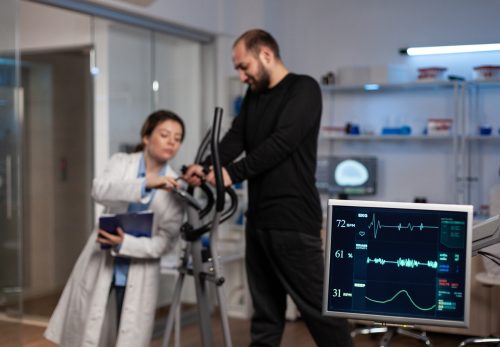 Specialist researcher doctor discussing with sportman in gym training equipment monitoring body endurance during medical workout in modern laboratory. Researcher doctor analyzing EKG data